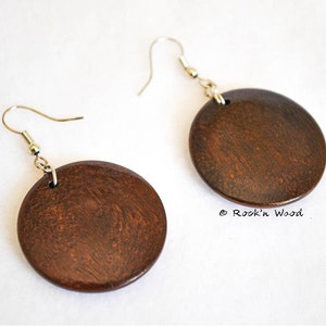 May include: A pair of brown wooden circle earrings with silver hooks. The earrings have a wood grain pattern and a glossy finish.