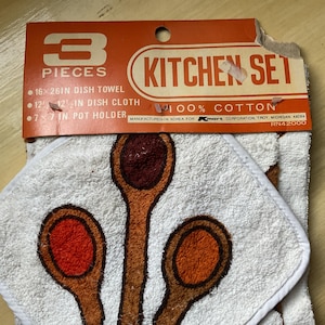 May include: A vintage kitchen set with a dish towel, dish cloth, and pot holder. The white cotton items feature a design of brown and orange spoons. The packaging reads "Kitchen Set" and "100% Cotton."