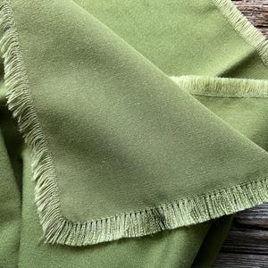 May include: A green fabric with a fringed edge. The fabric is folded in half and the fringed edge is visible on both sides.