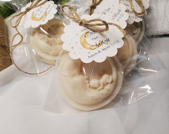 May include: Several soaps shaped like a crescent moon cradling a baby, packaged in clear cellophane. Each soap is tied with twine and a tag that reads "We Love You to the Moon" with a date and names.