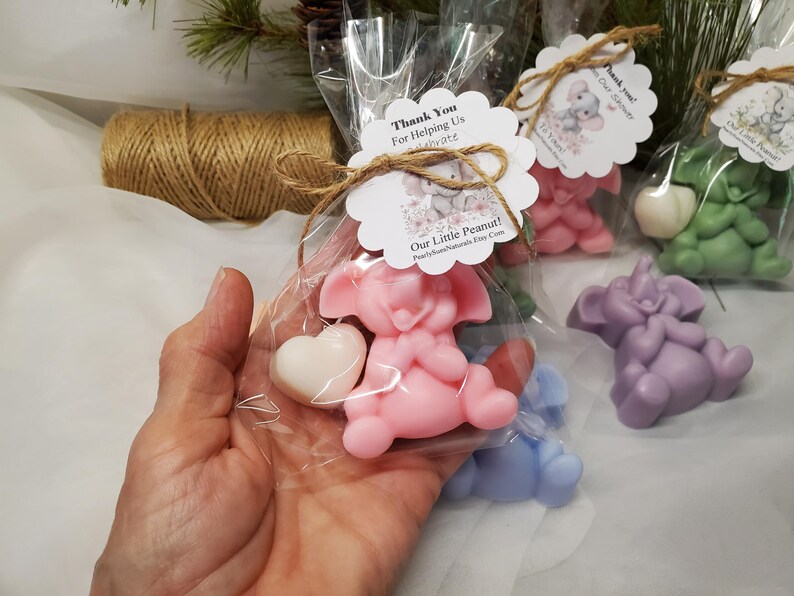 May include: Pink, purple, green, and blue elephant-shaped soaps, each holding a white heart. The soaps are packaged in clear cellophane bags, tied with twine, and adorned with a tag that reads "Our Little Peanut!"