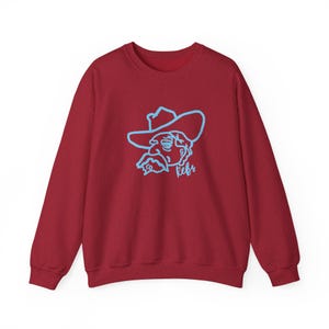 May include: A maroon sweatshirt featuring a light blue outline of a cowboy's face and hat. The word "Refs" is written in light blue below the image. The sweatshirt has long sleeves and a crew neck.