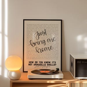 Peut inclure: Une affiche encadrée avec le texte « Just bring me home » et un tourne-disque avec un disque vinyle sur une étagère en bois. Une lampe sphérique avec une base blanche est à gauche. Une chaîne stéréo noire et blanche est à droite.