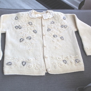 Cárdigan de punto vintage color crema con cuello de encaje, bordado floral y motivo de hojas con cuentas brillantes.