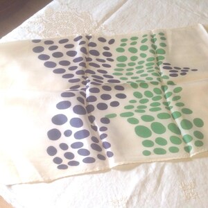 Puede incluir: Un pa&ntilde;uelo color crema con un estampado de lunares azul marino y verde. Los lunares est&aacute;n dispuestos en un patr&oacute;n disperso sobre la tela. El pa&ntilde;uelo est&aacute; doblado y parece estar hecho de un material ligero.