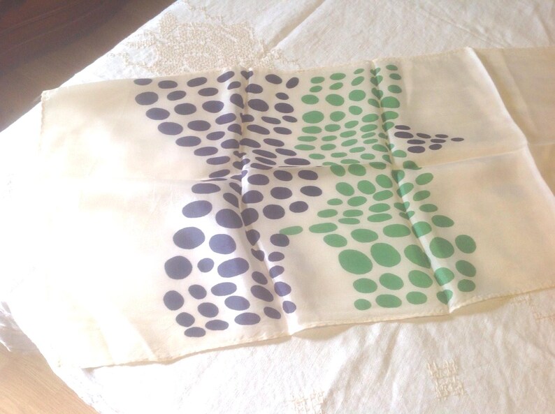 Puede incluir: Un pa&ntilde;uelo color crema con un estampado de lunares azul marino y verde. Los lunares est&aacute;n dispuestos en un patr&oacute;n disperso sobre la tela. El pa&ntilde;uelo est&aacute; doblado y parece estar hecho de un material ligero.