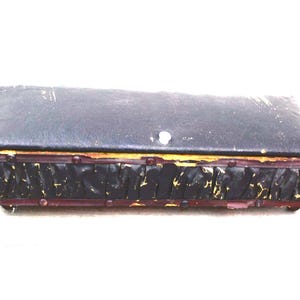 May include: A rectangular, antique black box with a hinged lid. The box has a distressed appearance with gold trim and a dark red base. The box is likely used for storage or display of small items.