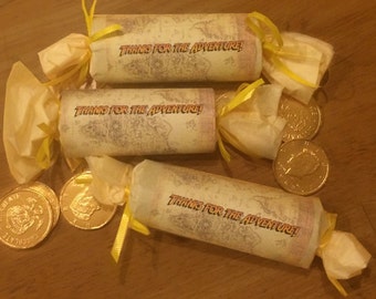 May include: Three yellow paper party favors with a map design and the text "Thanks for the adventure!"  Each favor is tied with a yellow ribbon and has a gold chocolate coin on top.