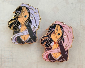 May include: Two enamel pins featuring a woman with black hair and a black and white outfit. One pin has a purple and white design, and the other has a pink and white design.
