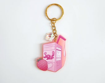 May include: Pink and white cartoon-style keychain featuring a carton of soy milk with a straw, a strawberry, and the word "Soy!" printed on the carton.