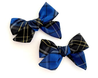 May include: Two blue and black plaid hair bows with yellow accents. The bows are tied in a knot and are ready to be worn in hair.