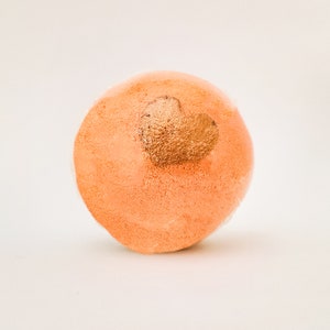 May include: A round orange bath bomb with a gold heart design.