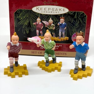 May include: Set of three Hallmark Keepsake ornaments featuring characters from The Wizard of Oz. Each figurine stands on a yellow brick road base. The box is red with gold lettering and a green background.