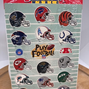 Peut inclure: Une feuille d'autocollants de casques d'équipes de la NFL. Les autocollants présentent une variété d'équipes, notamment les Patriots, les Jets, les Dolphins et les Raiders. Les autocollants sont imprimés sur un fond blanc avec une bordure rayée bleue et blanche.