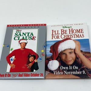 May include: Two VHS tapes for the movies "The Santa Clause" starring Tim Allen and "I'll Be Home for Christmas" starring Jonathan Taylor Thomas. Both tapes feature Christmas-themed artwork and release dates.