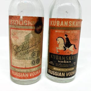 以下が含まれることがあります： 2つのヴィンテージロシアウォッカボトル。1つのボトルには「Stolichnaya Vodka」の文字と建物のイラストが描かれたラベルが付いています。もう1つのボトルには、馬に乗ったライダーと「Kubanskaya Vodka」の文字が描かれたラベルが付いています。