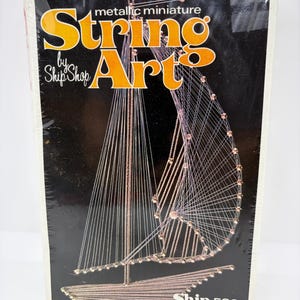May include: A sealed box for a metallic miniature String Art kit by Ship Shop featuring a graphic of a sailboat created with metallic thread and pins on a black background. The text reads String Art by Ship Shop, Ship 5801, and shown actual size.