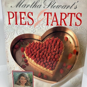 May include: A cookbook titled "Martha Stewart's PIES & TARTS" features a heart-shaped tart filled with strawberries. The cover has a photo of Martha Stewart and is labeled "Food & Entertaining Book."