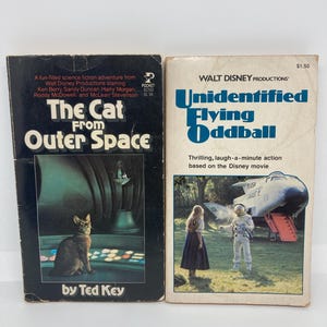 Peut inclure: Deux livres de poche vintage. Le premier, "The Cat From Outer Space", présente une illustration de chat. Le second, "Unidentified Flying Oddball", montre une scène avec un vaisseau spatial et des personnes. Les deux livres sont de Walt Disney Productions.