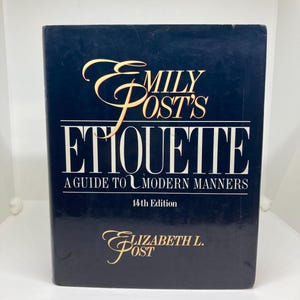 Op de afbeelding: Een donkerblauw hardback boek getiteld "Emily Post's Etiquette: A Guide to Modern Manners, 14th Edition" door Elizabeth L. Post.