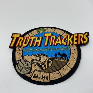 May include: Embroidered patch with the words "Truth Trackers" in yellow and red lettering. The patch features a blue background with additional text and illustrations of camels and a person. The text "John 14:6" is also included.