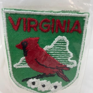 May include: Embroidered patch featuring a red cardinal bird and the word "VIRGINIA" in red letters. The patch has a green background with a white border and a white outline of mountains and flowers. The patch is in a clear plastic package.