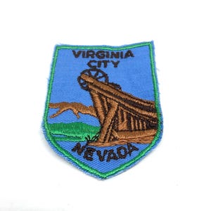 May include: A blue and green embroidered patch with the text "Virginia City, Nevada" and a brown image of a building with a large wheel.