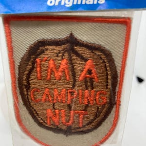 May include: Embroidered patch with the text "I'M A CAMPING NUT" in orange thread. The patch features a brown nut design with an orange border and a tan background. The word "originals" is visible at the top.