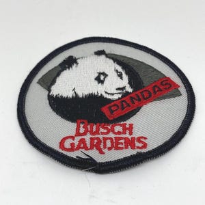 May include: Embroidered patch featuring a panda bear with the text "PANDAS" on a red banner. The patch also includes "BUSCH GARDENS" in red lettering, set against a gray and black circular background.