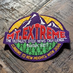 Pode incluir: Patch bordado roxo e dourado com o texto "MT. EXTREME" em vermelho, apresentando um design de montanha. O patch inclui as frases "THE ULTIMATE GOOD NEWS CHALLENGE" e "CLIMBING TO NEW HEIGHTS WITH JESUS".