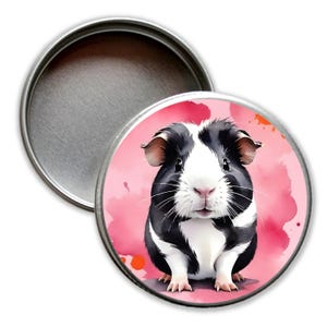 Könnte beinhalten: Eine runde, silberne Dose mit einer Aquarellillustration eines Meerschweinchens. Das Meerschweinchen ist schwarz und weiß mit rosa Nase und Ohren, vor einem rosa und orangefarbenen Aquarellhintergrund.