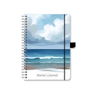 Könnte beinhalten: Ein blaues und weißes Spiralbuch mit einer Strandszene auf dem Cover. Das Cover zeigt ein blaues Meer mit weißen Wellen und einen bewölkten Himmel. Der Text "Marita's Journal" ist unten auf dem Cover gedruckt.