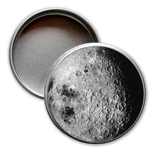 Könnte beinhalten: Eine runde Metalldose mit einem Schwarzweißbild des Mondes auf dem Deckel. Die Dose ist geöffnet und das Innere ist sichtbar.