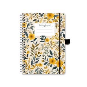 Könnte beinhalten: Ein spiralgebundenes Notizbuch mit einem floralen Design mit gelben Blumen und grünen Blättern auf cremefarbenem Hintergrund. Das Notizbuch hat einen schwarzen Gummizugverschluss und den Text "Sabines Journal" auf dem Einband.