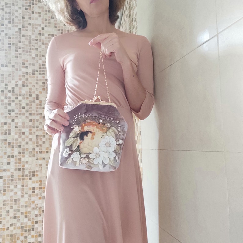 Puede incluir: Un peque&ntilde;o bolso de terciopelo gris con un dise&ntilde;o floral y una correa de cadena. El bolso est&aacute; decorado con cuentas y lentejuelas.
