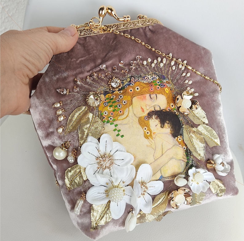 Puede incluir: Un bolso de mano de terciopelo con cierre y cadena de metal dorado. El bolso est&aacute; decorado con flores bordadas, perlas y una pintura de una madre y un ni&ntilde;o.