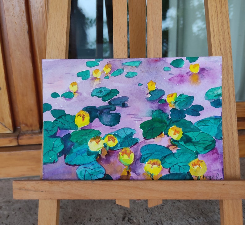 May include: Watercolor painting of yellow water lilies on a purple background. The lilies are surrounded by green lily pads and leaves. The painting is signed "7U Hangut O."