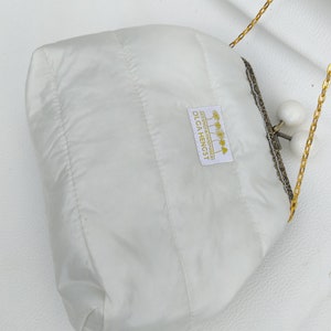 May include: White quilted clutch bag with a gold chain strap and a white label that reads "DESIGNED & HANDMADE BY OLGA HENGST".