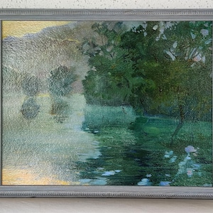 May include: A framed painting depicting a tranquil forest scene with a lake in the foreground. The trees are a vibrant green, and the water is a calming blue-green. The painting is framed in a simple gray frame.