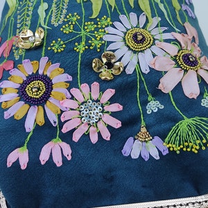 K&ouml;nnte beinhalten: Eine Clutch aus blaugr&uuml;nem Samt mit goldenem Metallrahmen und Kette. Die Clutch ist mit bunten Blumen und Perlen bestickt.