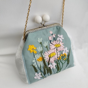 May include: A light blue fabric purse with a white clasp and a floral embroidery design. The flowers are embroidered in shades of yellow, pink, and white.