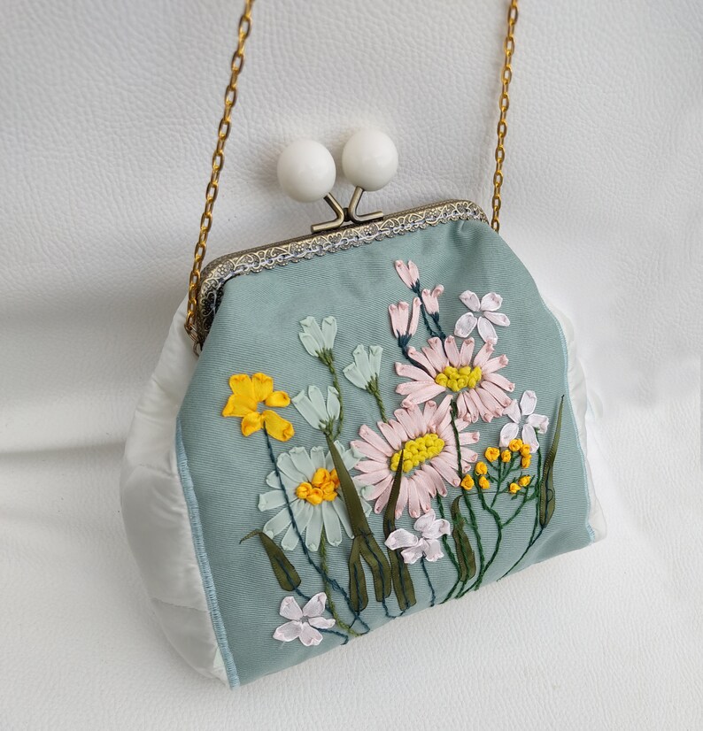 May include: A light blue fabric purse with a white clasp and a floral embroidery design. The flowers are embroidered in shades of yellow, pink, and white.