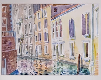 Puede incluir: Pintura acuarela de un canal en Venecia, Italia. La pintura representa un canal estrecho con edificios que bordean ambos lados. Los edificios están pintados en tonos de amarillo, blanco y marrón. El agua del canal es de color azul claro y refleja los edificios y el cielo. La pintura está firmada en la esquina inferior derecha.
