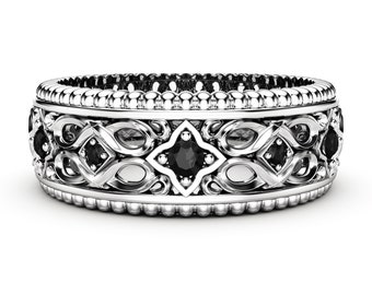 May include: A silver ring with an intricate design featuring black gemstones. The ring has a detailed pattern of interwoven shapes and small, round beads along the edges. The gemstones are set in a symmetrical arrangement.