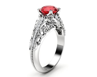 Puede incluir: Un anillo de plata con una gran piedra roja rodeada de piedras blancas más pequeñas. El anillo tiene un diseño detallado y ornamentado.
