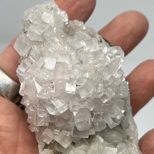 May include: A cluster of white calcite crystals with a rough, natural texture. The crystals are arranged in a layered formation, creating a unique and interesting display.