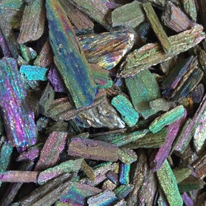 May include: A close-up of iridescent, metallic, and glittery, dark gray, blue, and green, flat, irregular shaped pieces of mica.