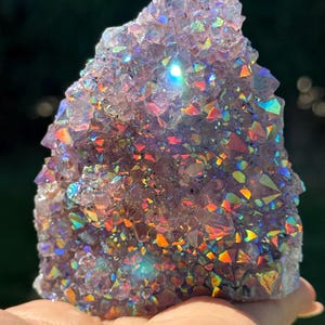 以下が含まれることがあります： 紫色の結晶の先端に虹のような金属光沢を生み出す、虹色のオーラコーティングが施されたアメジストの結晶クラスター。この鉱物形成は、光を反射する多数の鋭く多面的な結晶の先端を特徴としています。