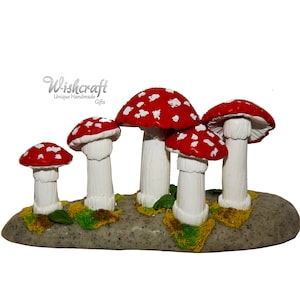 Puede incluir: Un grupo de cinco figuritas de setas rojas y blancas con tallos blancos, dispuestas sobre una base de roca gris. Las setas están agrupadas, creando una exhibición caprichosa y encantadora.