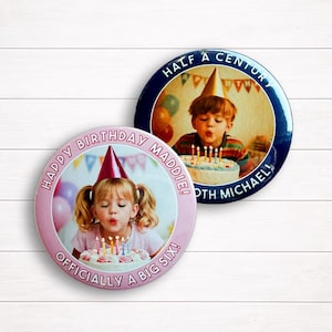 May include: Two circular pin-back buttons featuring birthday photos. The pink button displays a child blowing out candles with the text "HAPPY BIRTHDAY MADDIE! OFFICIALLY A BIG SIX!". The dark blue button shows a child with "HALF A CENTURY 50TH MICHAEL!".
